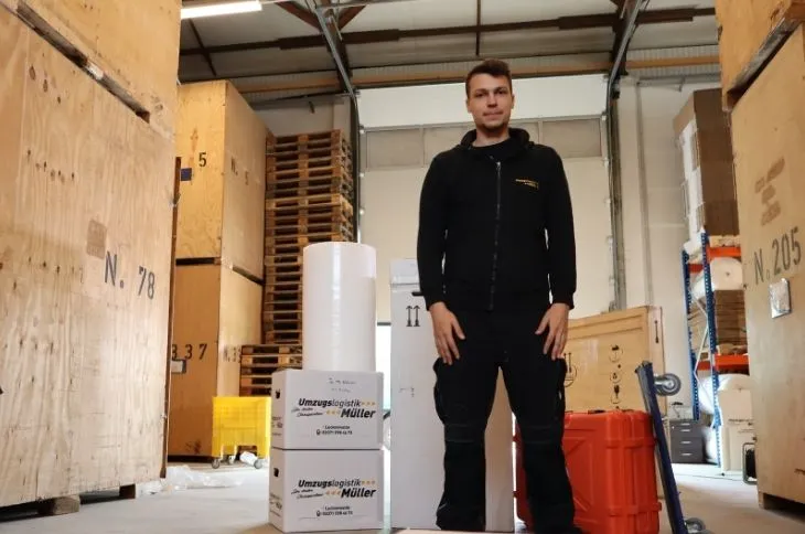 umzugshelfer steht zwischen umzugskartons und transportmaterial